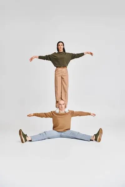 Acrobatic couple in casual attire, young woman standing on shoulders of man on grey background — Stock Photo