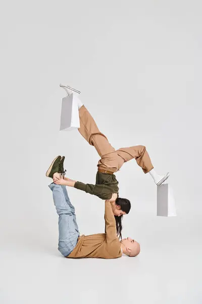 Акробатична пара, молода жінка з сумками на ногах балансує з підтримкою чоловіка в студії — стокове фото