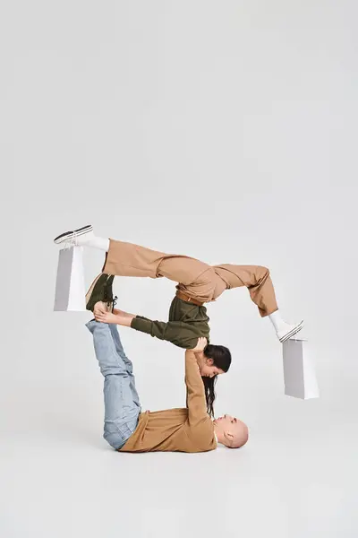 Coppia acrobatica, donna con shopping bag su gambe bilanciate con supporto dell'uomo in studio — Foto stock