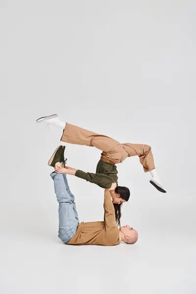Akrobatisches Paar, junge brünette Frau in lässiger Kleidung balanciert mit Unterstützung eines Mannes im Studio — Stockfoto