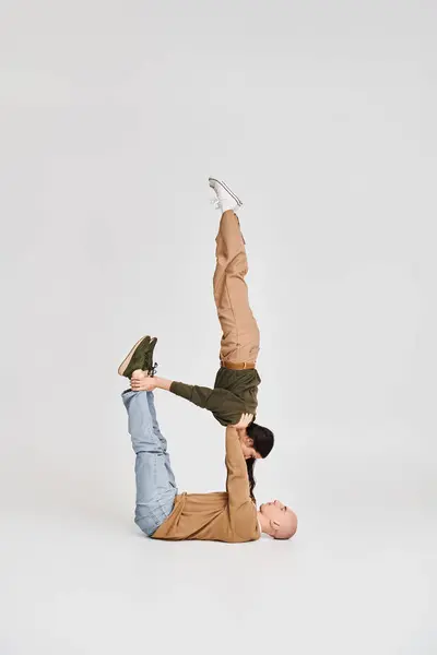Akrobatisches Paar, junge brünette Frau in lässiger Kleidung balanciert mit Unterstützung ihres Partners auf grau — Stockfoto