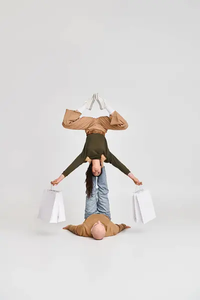 Junges Paar, akrobatische Frau hält Einkaufstüten in der Hand und balanciert mit Unterstützung des Partners — Stockfoto