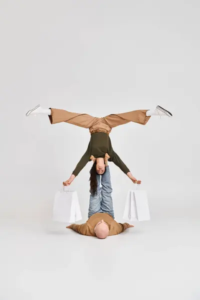 Coppia artistica, donna acrobatica in possesso di borse della spesa e bilanciamento con il supporto dell'uomo in studio — Foto stock