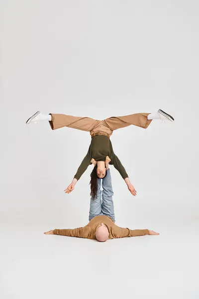 Casal artístico, mulher acrobática segurando equilíbrio de cabeça para baixo com o apoio do homem no estúdio cinza — Fotografia de Stock