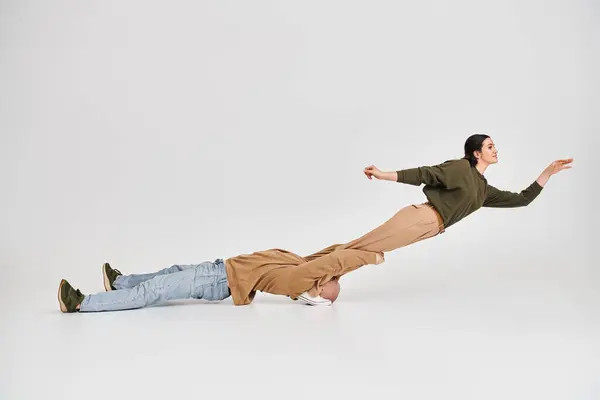 Akrobatische Frau in Freizeitkleidung balanciert in der Luft mit Unterstützung ihres Partners im Studio auf grau — Stockfoto
