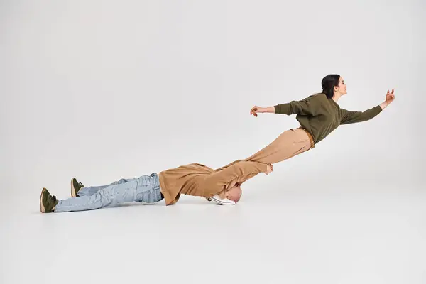 Акробатична жінка в повсякденному носінні балансує в повітрі за підтримки свого партнера в сірій студії — стокове фото