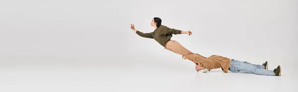 Акробатична жінка в повсякденному носінні балансує в повітрі за підтримки свого партнера в сірій студії, банер — стокове фото