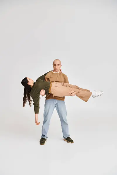 Man in casual attire holding in arms beautiful brunette woman on grey background, young couple — Stock Photo