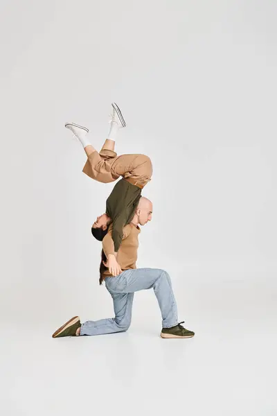 Donna bruna in equilibrio a testa in giù con il supporto dell'uomo in abbigliamento casual durante le prove in studio — Foto stock