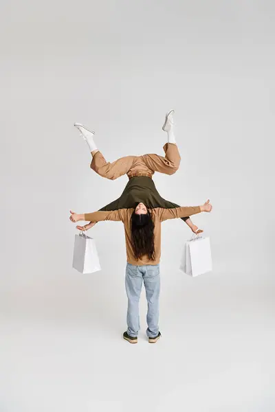 Mulher segurando sacos de compras e equilibrando de cabeça para baixo com o apoio do parceiro acrobático no estúdio — Fotografia de Stock