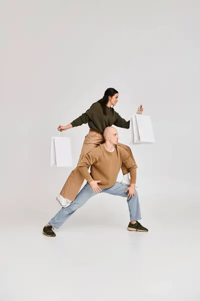 Acrobatica performance di giovane coppia, donna con shopping bag in equilibrio sul corpo dell'uomo su grigio — Foto stock