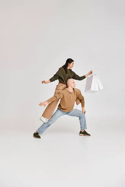 Performance acrobatica di coppia artistica, donna con shopping bag in equilibrio sul corpo dell'uomo su grigio — Foto stock
