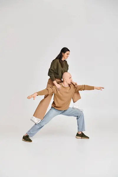 Acrobatic performance of artistic couple, woman in casual clothes balancing on legs of man on grey — Stock Photo