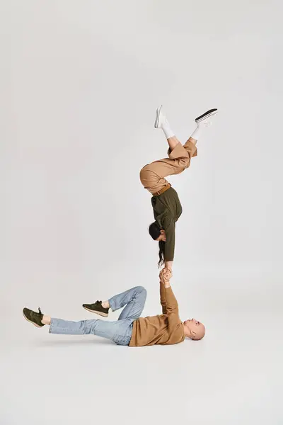 Actuación acrobática de pareja artística, mujer en ropa casual equilibrio en las manos del hombre en gris - foto de stock