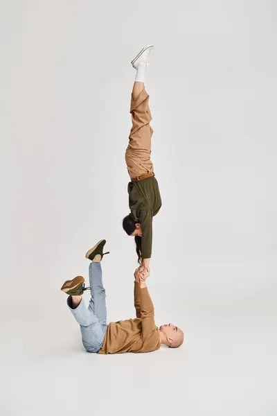 Actuación acrobática de pareja artística, mujer en ropa casual equilibrio en las manos del hombre en gris - foto de stock