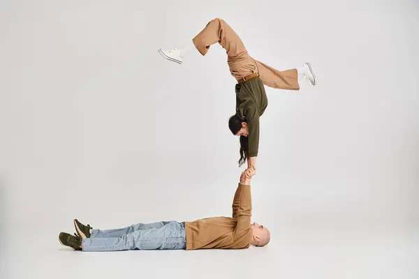 Akrobatische Darbietung eines künstlerischen Paares, Frau in Freizeitkleidung balanciert auf den Händen eines Mannes auf grau — Stockfoto