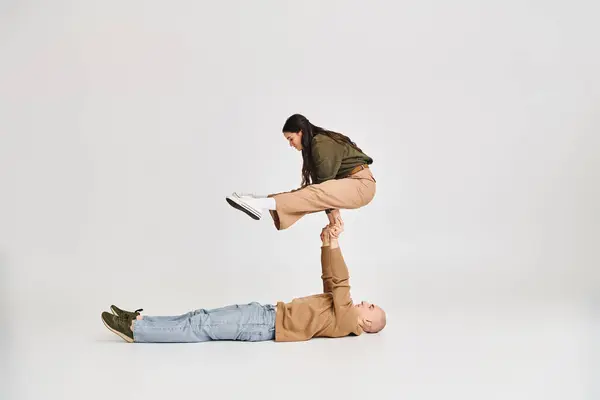 Acrobatic performance of young couple, woman in casual clothes balancing on hands of man on grey — Stock Photo