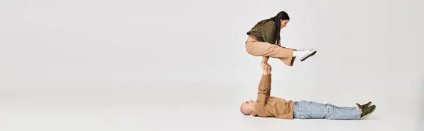 Performance von künstlerischem Paarbanner, Frau in lässiger Kleidung balanciert auf Händen von Mann auf Grau — Stockfoto