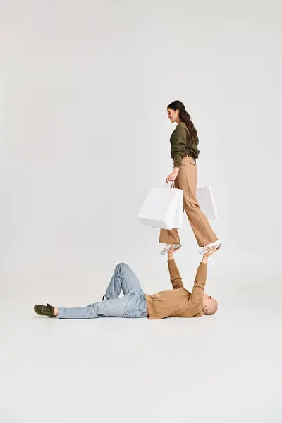 Giovane donna in abbigliamento casual tenendo borse della spesa e bilanciamento delle mani su uomo forte, acrobati — Foto stock