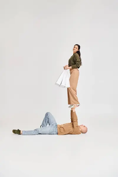 Жінка в повсякденному одязі тримає сумки і балансує на руках сильного чоловіка, пара акробатів — стокове фото