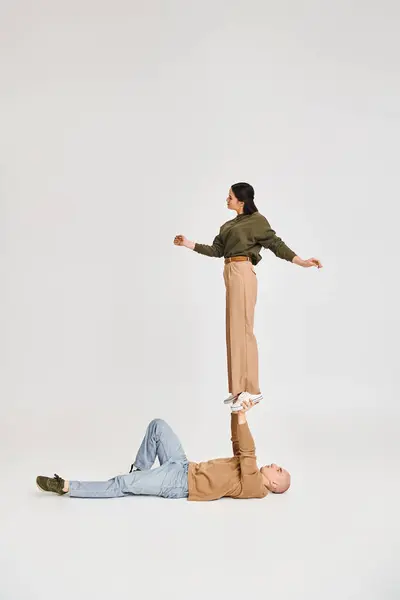 Jovem morena em casual desgaste balanceamento em mãos de homem forte, casal de acrobatas em estúdio — Fotografia de Stock