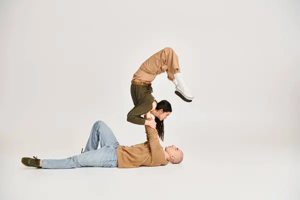 Giovane donna bruna in abbigliamento casual bilanciamento sulle mani di uomo forte, coppia di acrobati in studio — Foto stock