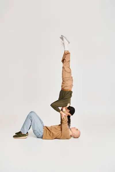 Brünette Akrobatin in Freizeitkleidung balanciert auf den Händen eines starken Mannes, Paar probt im Studio — Stockfoto