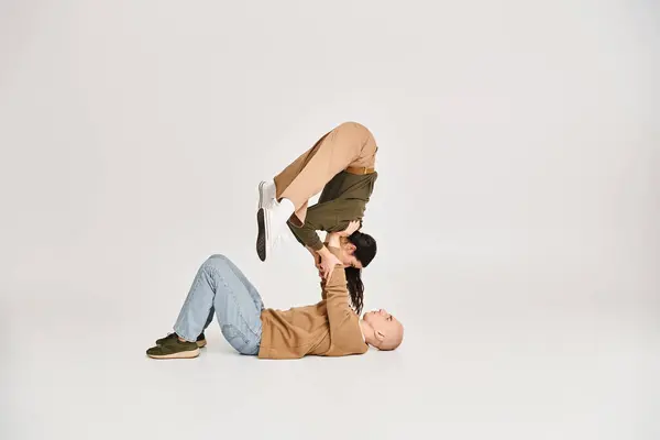 Giovane donna bruna in abbigliamento casual bilanciamento sulle mani di uomo forte, coppia di acrobati in studio — Foto stock