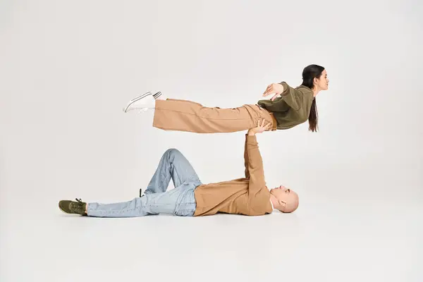 Homme fort en tenue décontractée couché sur le sol et levant femme brune en studio, couple d'acrobates — Photo de stock