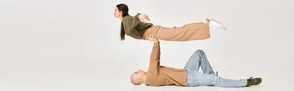 Uomo in abbigliamento casual sdraiato sul pavimento e sollevamento donna bruna in studio, coppia di acrobati banner — Foto stock