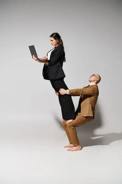 Mujer en traje de negocios con portátil balanceo en vueltas de hombre en traje en gris, par de acróbatas - foto de stock