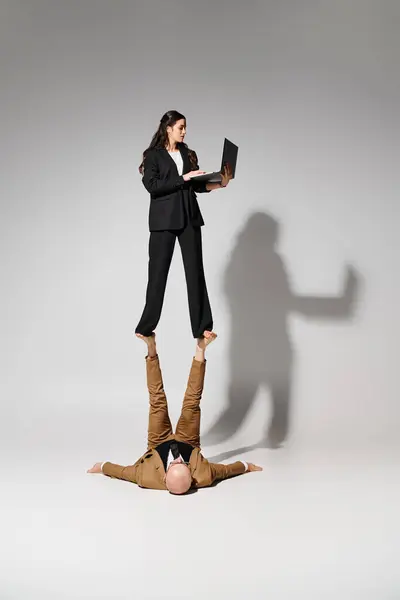 Mulher em traje de negócios com laptop balanceamento em pés de homem desgaste formal, par de acrobatas — Fotografia de Stock