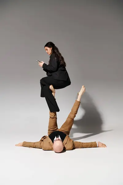 Businesswoman with smartphone sitting on feet of man in suit on grey, couple of acrobats — Stock Photo