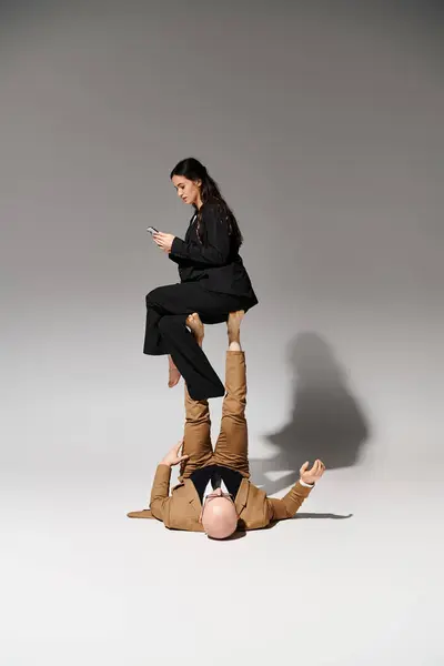 Jeune femme d'affaires avec smartphone équilibrage sur les pieds de l'homme en costume sur gris, couple d'acrobates — Photo de stock