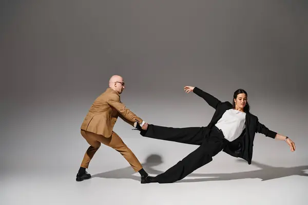Ballerini dinamici in abiti da lavoro che eseguono un atto di bilanciamento in uno studio con sfondo grigio — Foto stock