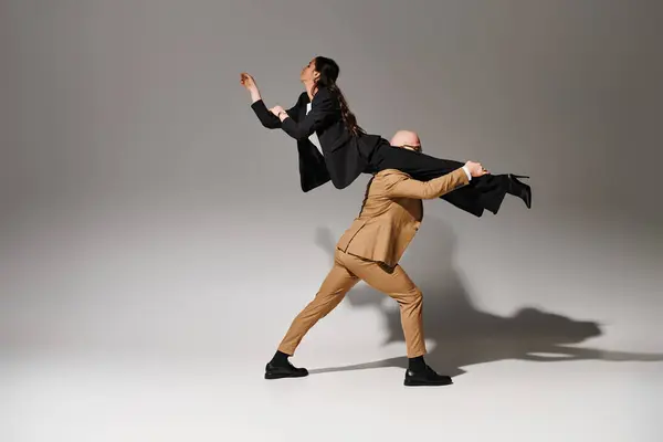 Чоловік в офіційному вбранні ліфтинг брюнетка і витончена жінка в костюмі балансування під час танцю в студії — стокове фото