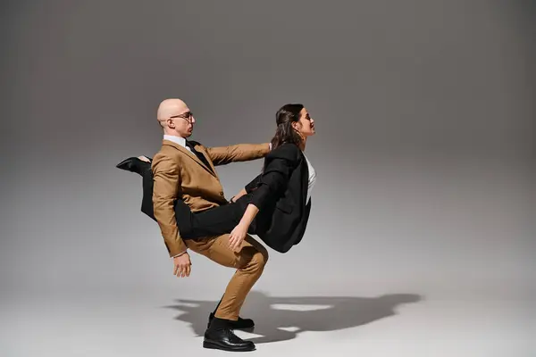Dynamic dancers in business attire performing a balancing act in a studio with grey background — Stock Photo