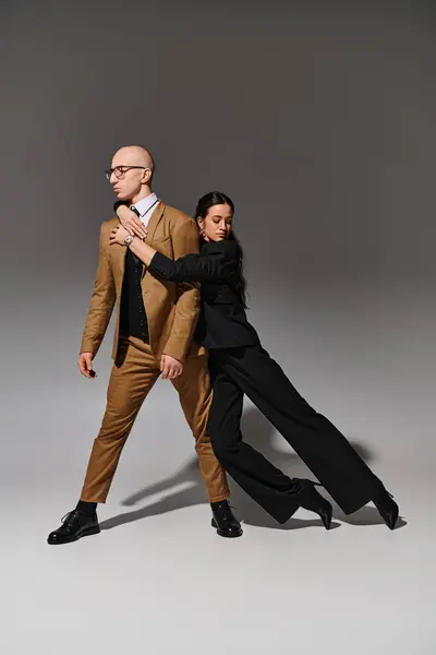 Elegante pareja en traje de negocios realizando un paso de baile en el estudio sobre fondo gris, soporte - foto de stock