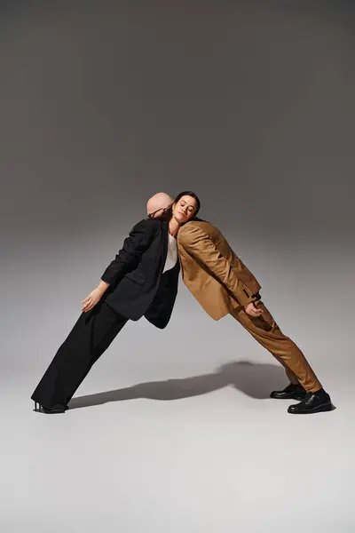 Jeune couple artistique en tenue de travail effectuant un mouvement de danse miroir en studio avec fond gris — Photo de stock