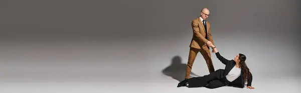 Hombre de la mano de la mujer en ropa formal mientras realiza movimiento de baile en el estudio de gris, pancarta - foto de stock