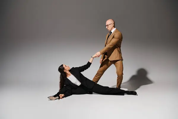 Akrobatin in eleganten Corporate Anzügen, die einen Spagat vollzieht und Händchen hält mit Mann im Studio — Stockfoto
