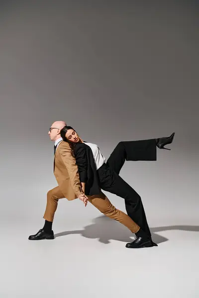 Pareja de baile en movimiento coordinado, mujer de traje apoyada en la espalda del hombre en traje de negocios en gris — Stock Photo
