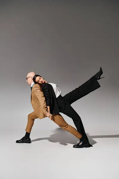 Партнеры по согласованному танцевальному движению, женщина в костюме, опирающаяся на мужчину в деловой одежде на серого — стоковое фото