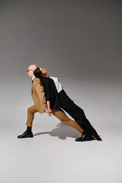 Parejas en movimiento de baile, mujer en traje apoyado en la espalda del hombre en traje de negocios en el fondo gris — Stock Photo