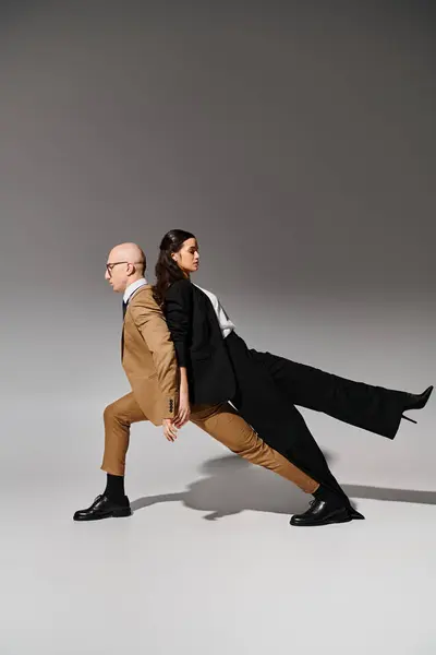 Couple in dancing move, woman in suit leaning on back of man in business attire on grey backdrop — Stock Photo