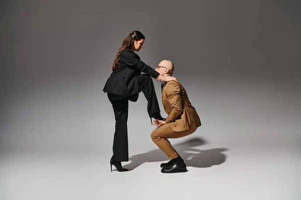 Брюнетка женщина балансирует на высоких каблуках, наступая на руку танцора в костюме на сером — стоковое фото