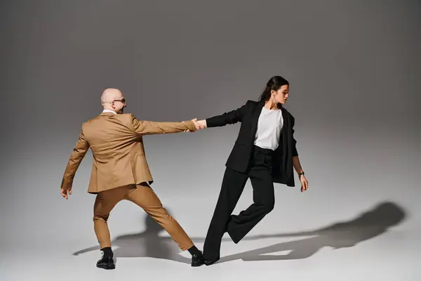 Pareja de baile en ropa formal tomados de la mano durante la actuación en estudio con fondo gris - foto de stock