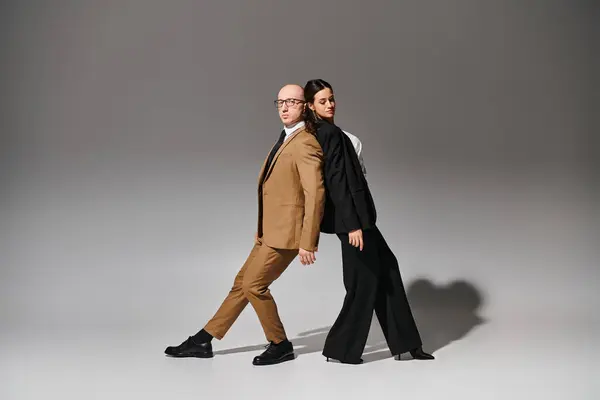 Young artistic couple in business attire performing a mirror dance move in studio with grey backdrop — Stock Photo