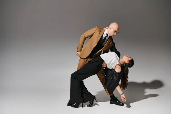 Brunette woman in formal wear bending with support of man in glasses on grey background — Stock Photo