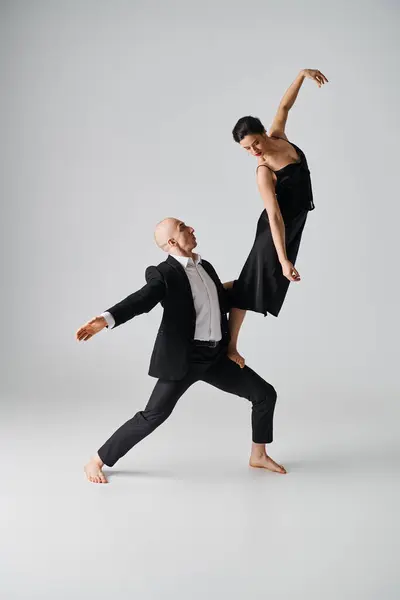 Femme pieds nus en robe noire équilibrant gracieusement sur le tour de partenaire de danse en studio gris — Photo de stock